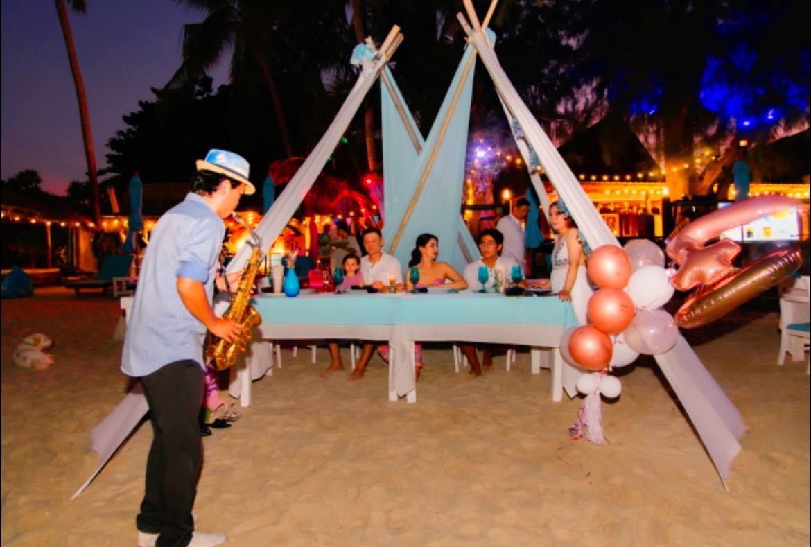 Saxophonist serenading the table under the tents — balloons, lights, full celebration setup