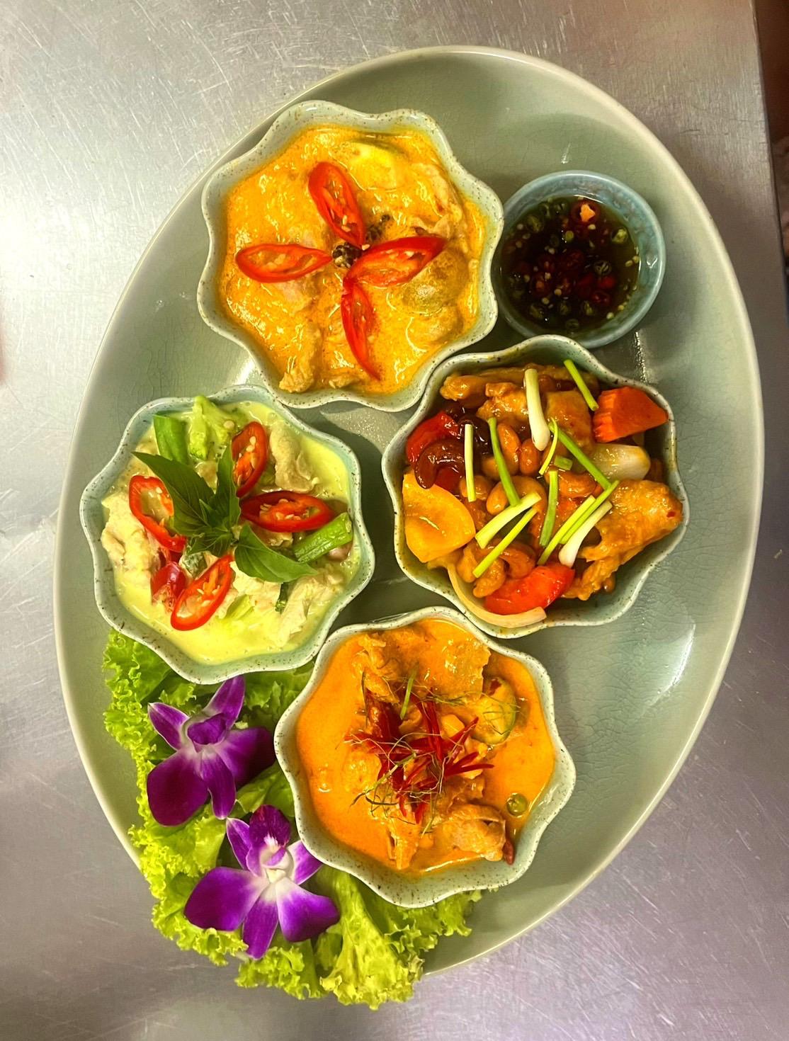 Tasting platter — green curry, panang, cashew stir-fry served in ceramic bowls with orchid garnish