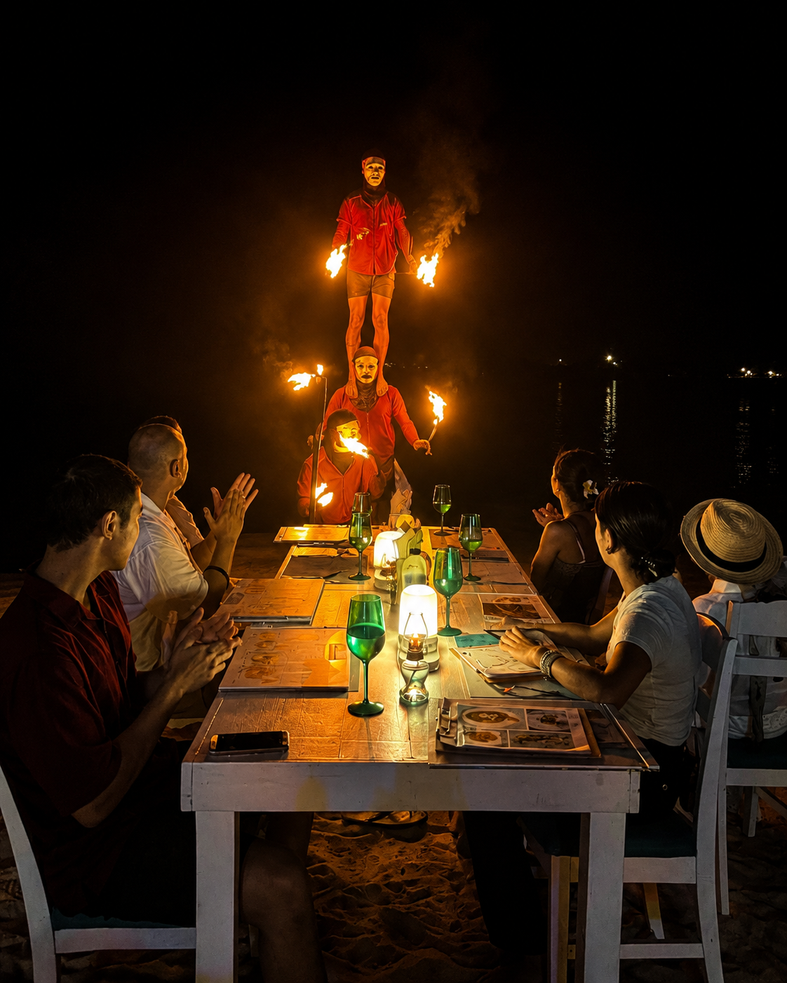 Fire performers directly beyond an occupied beachfront dining table at night
