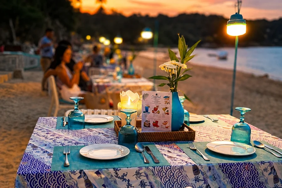 Blue-patterned beachfront dining table with flowers and a lantern at dusk