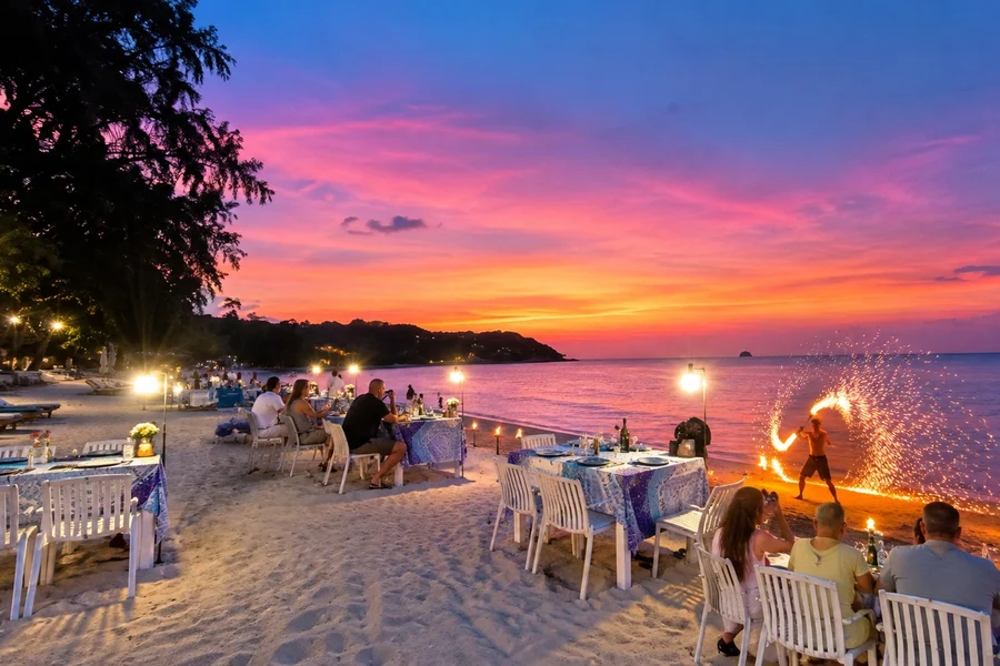 Beachfront dining tables and a fire performer beneath a pink sunset at The Blue Spice