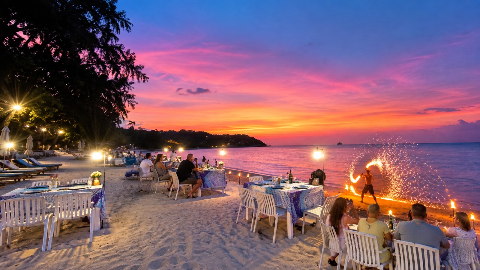 Beachfront dining tables and a fire performer beneath a pink sunset at The Blue Spice