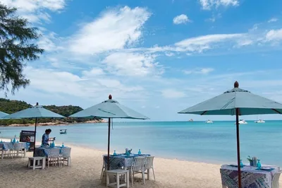 Lunch tables in the sand under parasols at The Blue Spice Samui on Choeng Mon Beach
