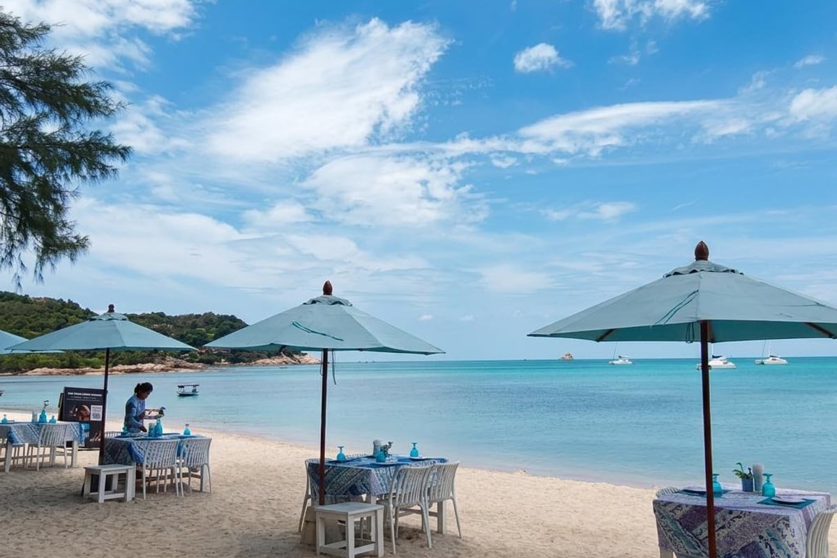 Lunch tables in the sand under parasols at The Blue Spice Samui on Choeng Mon Beach