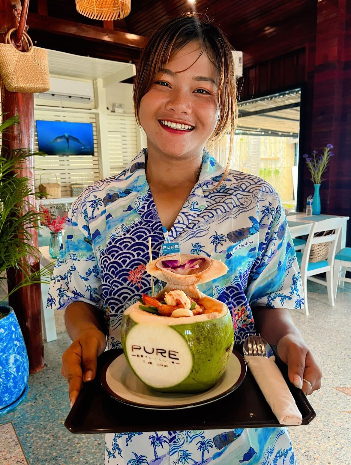 Smiling staff serving a signature coconut dish — beachside hospitality at its best